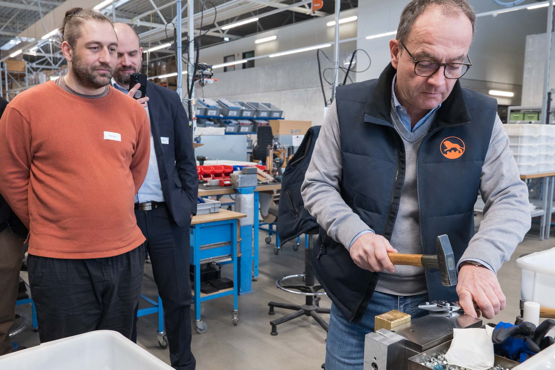 Randolph Schröder baut in einer Werkstatt eine Schere zusammen, während zwei KI.SH-Mitarbeitende zuschauen